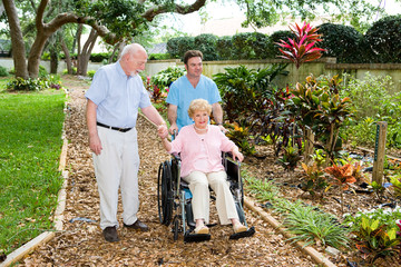 Senior woman in a wheelchair being walked through garden