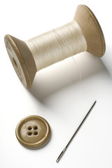 a spool of thread, needle and button on white