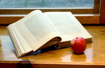 The open book and red apple on a window sill.