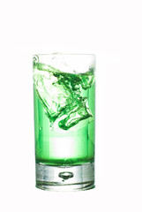 Eiswürfel fällt in ein Glas mit Waldmeistersyrup