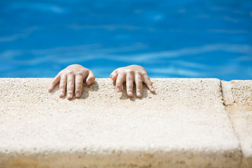 Small hands holding onto the edge of a swimming pool