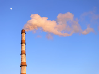 Smoking factory pipe in the sunset over the blue sky