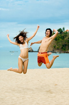 Two young adults jumping in the air on the beach