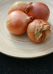 Four organic onions set on a round wooden plate.
