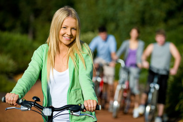 Obraz premium A young woman on a bike with group of friends in background