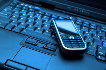 Blue-toned keyboard of laptop and modern smartphone on it.