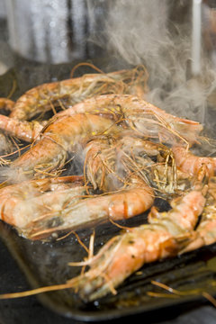 Smoking prawns cooking on an iron barbecue plate.