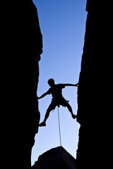 Rock climber silhouetted as he climbs up a chimney.