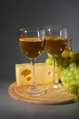 Two glasses of wine, cheese and grapes on a wooden board