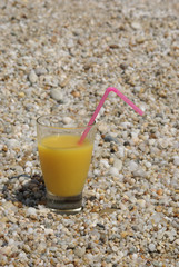 Glass with juice and straw on a beach