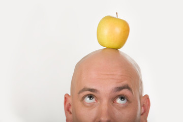 Close-up of bald male head with yellow apple on it