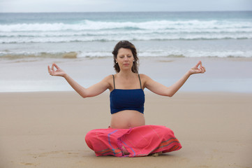 Fototapeta na wymiar Beautiful pregnant girl practicing yoga on the beach