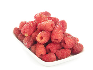 Several ripe raspberries at small plate isolated on white.