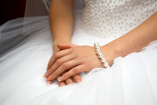 hands of fiancee are together on white dress