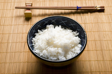 bowl of white fluffy rice with chopsticks and bamboo placemat