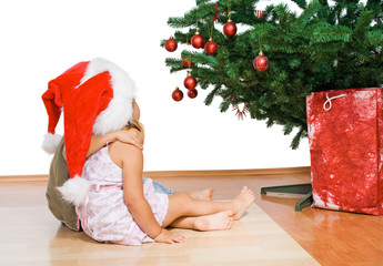 Kids sitting in front of the christmas tree hugging - isolated