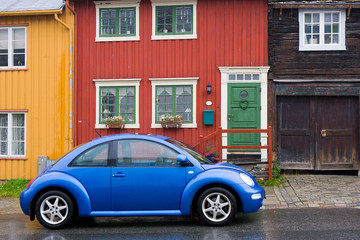 Fototapeta na wymiar blue car on old style wooden colorful houses background