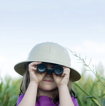 Young child looking through toy binoculars wearing safari hat