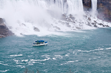 A boat sailing in a river next to Niagara falls