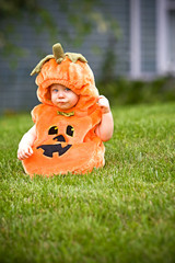 Baby in a halloween pumpkin costume sitting on grass