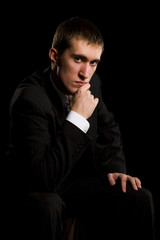 Young man sitting on black isolated background