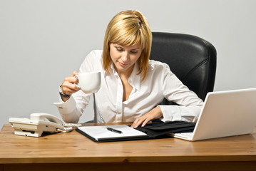 Business lady at a desk reading and drinking coffee.