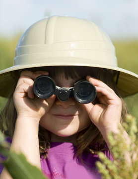 Young child looking through toy binoculars wearing safari hat