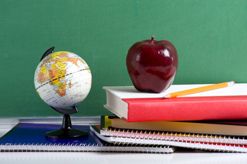 A stack of school books and an apple and a miniature globe