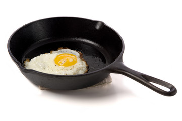 A fried egg in a black iron skillet on a white background