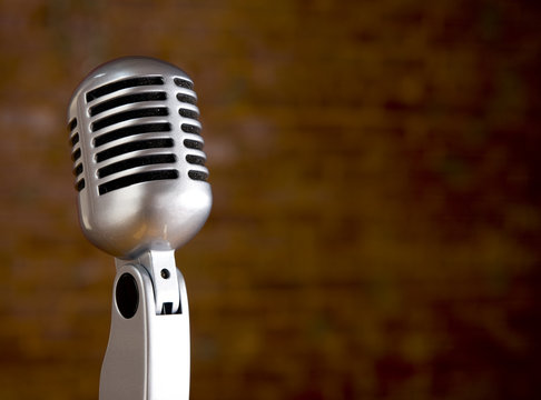 A silver vintage microphone in front of a blurred brick wall