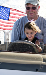 Little girl sitting in her grandfather's lap driving a boat