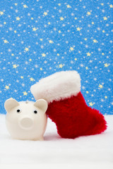 Piggy bank and red stocking sitting on snow, Christmas savings