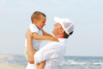 Portrait of young father holding son in his arms by seashore.