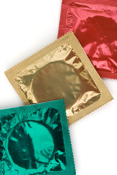 Three colourful condoms in their wrappers on white
