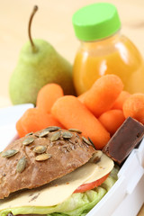 box with sandwich fruits and chocolate and bottle of juice