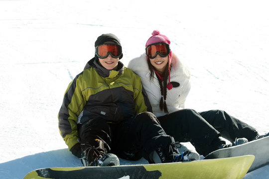 Young happy couple in goggles on snowboards