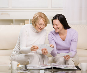 Adult mother and daughter enjoying photo album in livingroom
