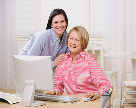 Adult mother and daughter posing with computer at home