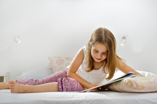 little girl lying on bed reading a book