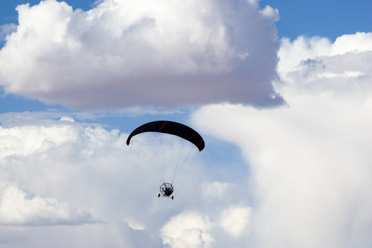 a powered paraglider pilot in flight with a cloudy sky