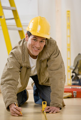 Worker in hard-hat kneeling and using measuring tape