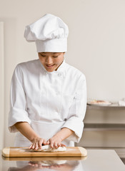 Chef  in toque and whites kneading dough in commercial kitchen