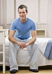 Confident man in pajamas sitting on bed in bedroom