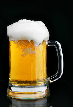 Mug of beer with froth over black background