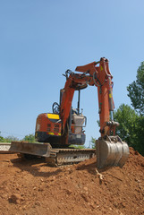 Fototapeta na wymiar Working with excavator on a heap of red ground