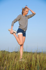 Athletics young woman stretching in a hilly meadow