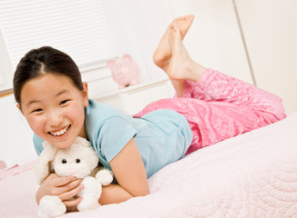 Happy, barefoot girl laying on bed with stuffed animal