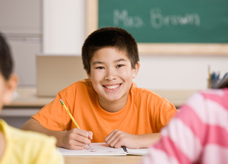 Happy student writing in notebook in school classroom