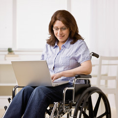 Disabled woman sitting in wheel chair typing on laptop