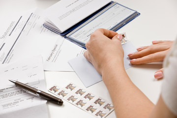 Woman writing checks from checkbook to pay monthly bills